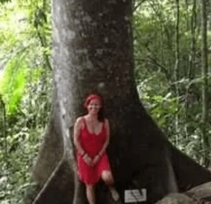 Isa Herrera outdoors, standing beside a large tree.