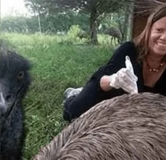 Isa Herrera crouched next to Morton, a friend's emu, outdoors.