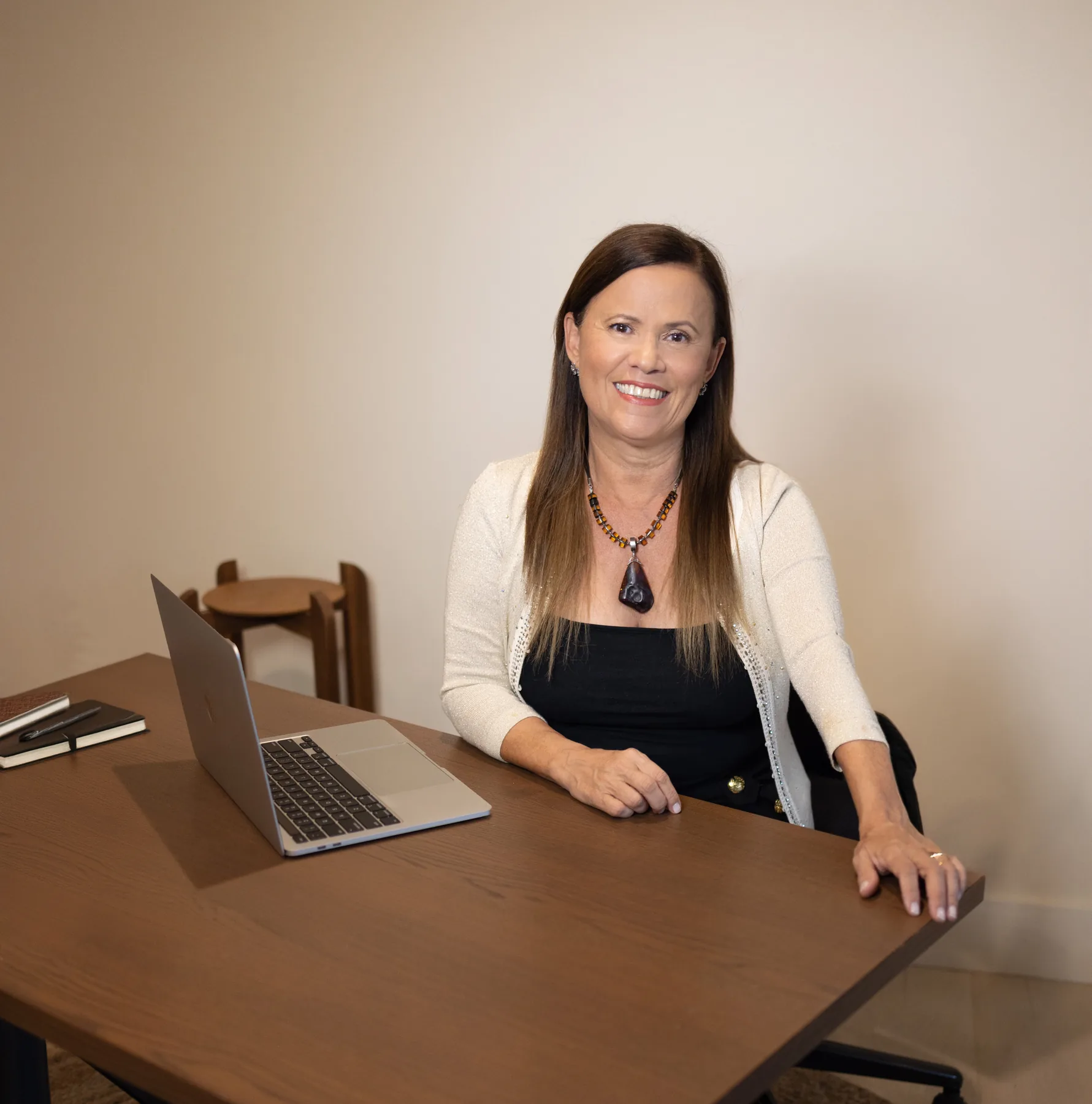 Isa Herrera, MSPT, CSCS, seated at her desk with an open laptop, wearing a cream cardigan against a warm neutral wall.