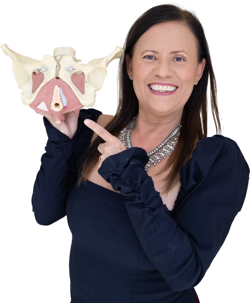 Isa Herrera holding an anatomical model of the pelvis with the muscle layer in pink, pointing at it and smiling.